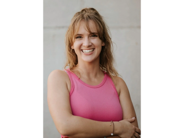 Smiling woman in a pink sleeveless top with arms crossed.