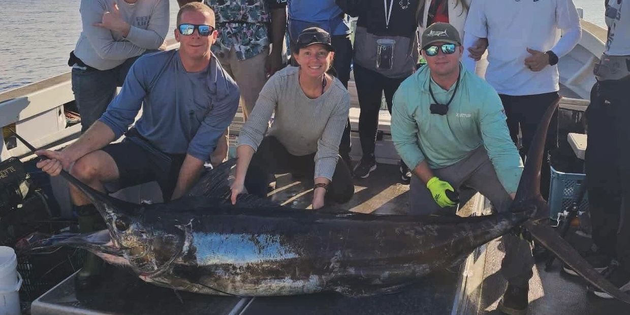 Group of anglers posing with a large marlin on a boat.