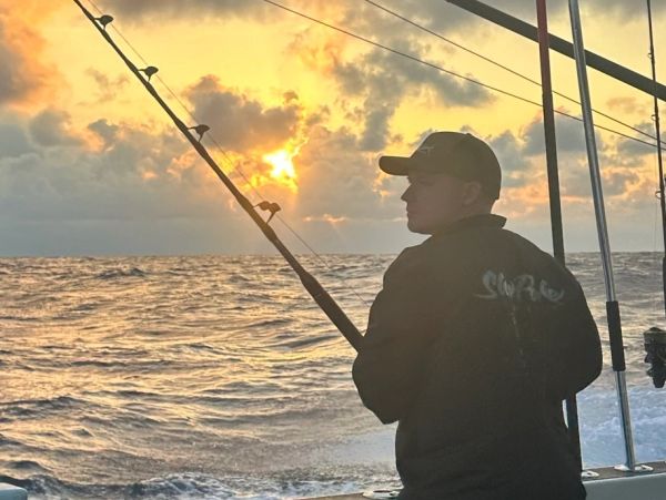 Person fishing on a boat at sunset over choppy waters.