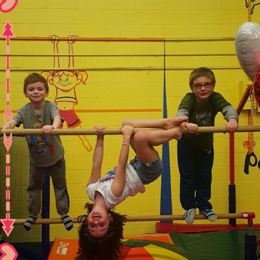 Three kids playing on a gym bar.