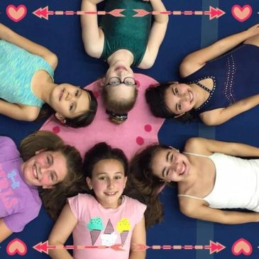 Six girls lying in a circle, smiling upward.