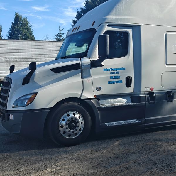 White semi-truck parked on gravel under a clear blue sky.