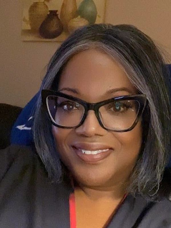 Woman with glasses smiling at the camera indoors.
