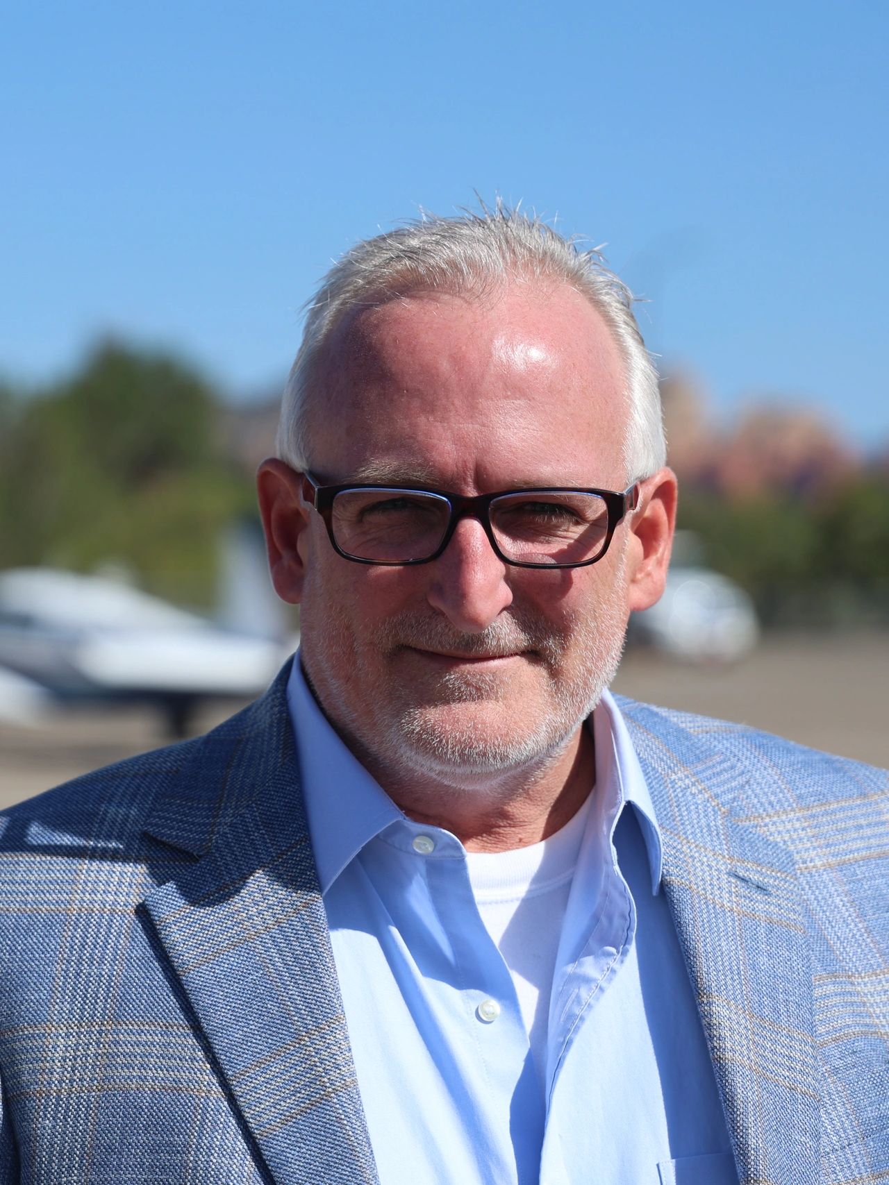 Middle-aged man with glasses in a blue suit jacket outdoors.