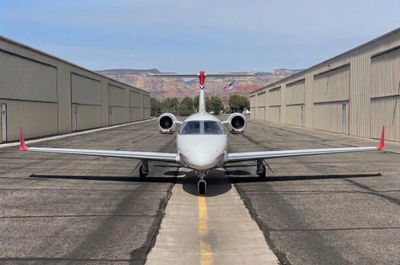 Front view of a small private jet on a runway between hangars.