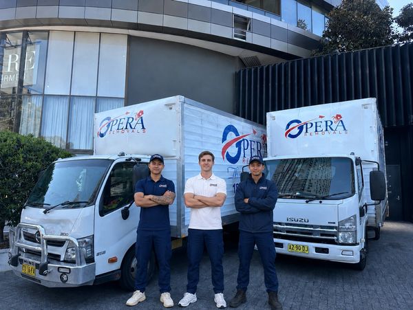 Three men standing confidently in front of Opera Removals trucks.