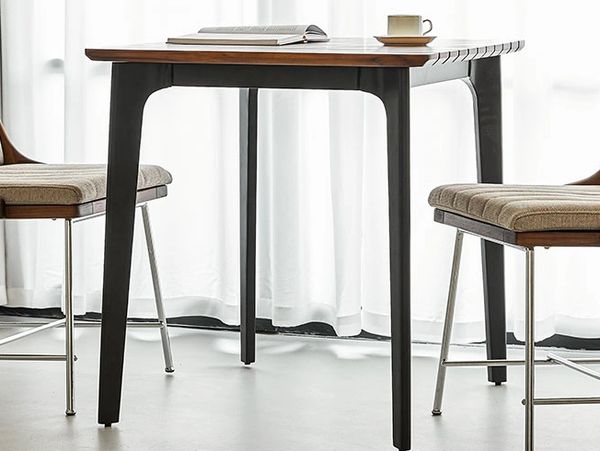 Modern wooden table with two cushioned chairs by a window with white curtains.