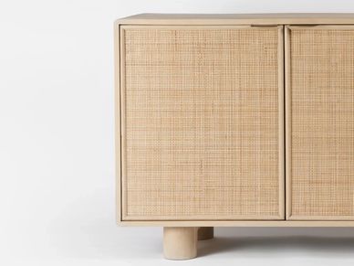 Close-up of a wooden cabinet with woven rattan doors and cylindrical legs.