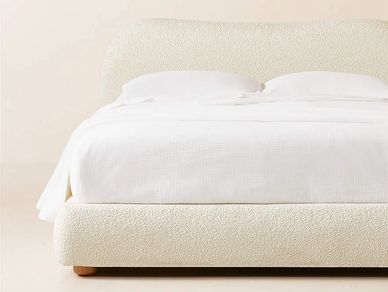 Minimalist bed with white bedding and a textured, cream-colored upholstered frame.