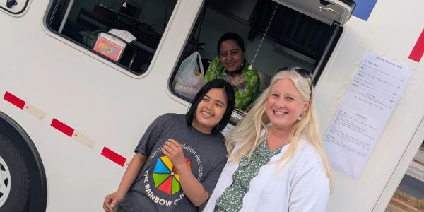 Three smiling women outside and inside a white vehicle, enjoying a sunny day.