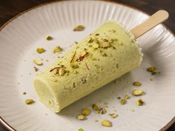 Pistachio ice cream bar with nuts on a white plate.