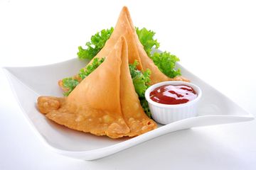 Two samosas with dipping sauce on a white plate.