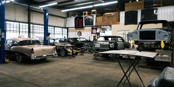 Restoration shop with cars in various build stages, including Camaro, Bel Air, Ford Truck
