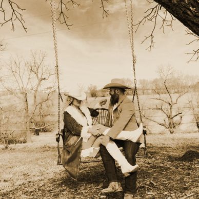 Couple in vintage western attire sharing a moment on a swing.