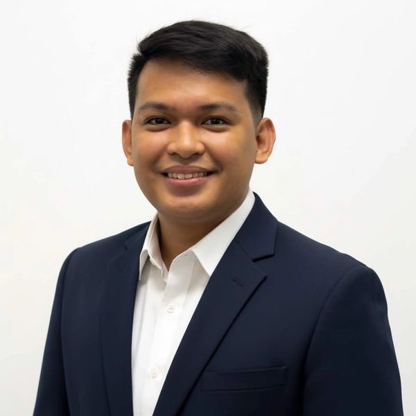 Young man in a navy suit smiling against a white background.