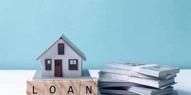 A miniature house on blocks spelling 'LOAN' next to stacks of money.