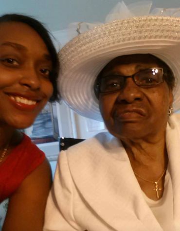 A young woman smiling next to an older woman in a white hat and glasses.