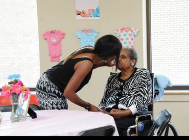 A young woman affectionately kisses an elderly woman in a wheelchair.