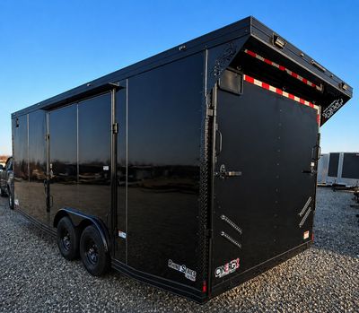 A sleek black enclosed trailer parked on gravel under a clear blue sky.