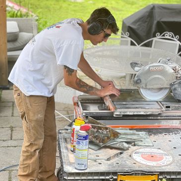 Man cutting tile using a wet saw, wearing ear protection.