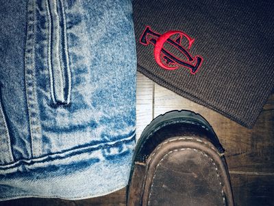 A flat lay of a denim jacket, an outdoor shoe, and a headgear