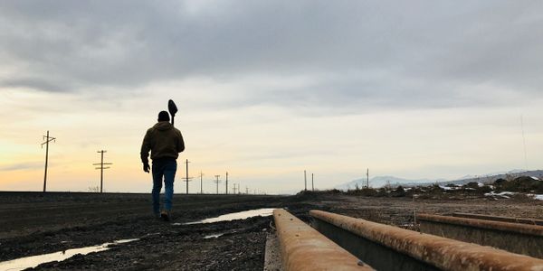 A person walking on a field path with a shovel in his shoulder