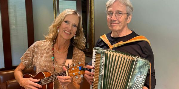 Two older adults playing musical instruments and smiling indoors.