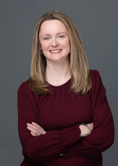 Smiling woman with arms crossed in maroon top.