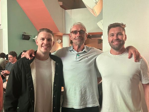Three men smiling together at a nighttime social gathering.