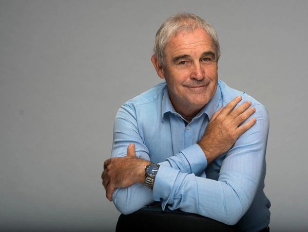 Smiling elderly man in blue shirt posing with crossed arms.