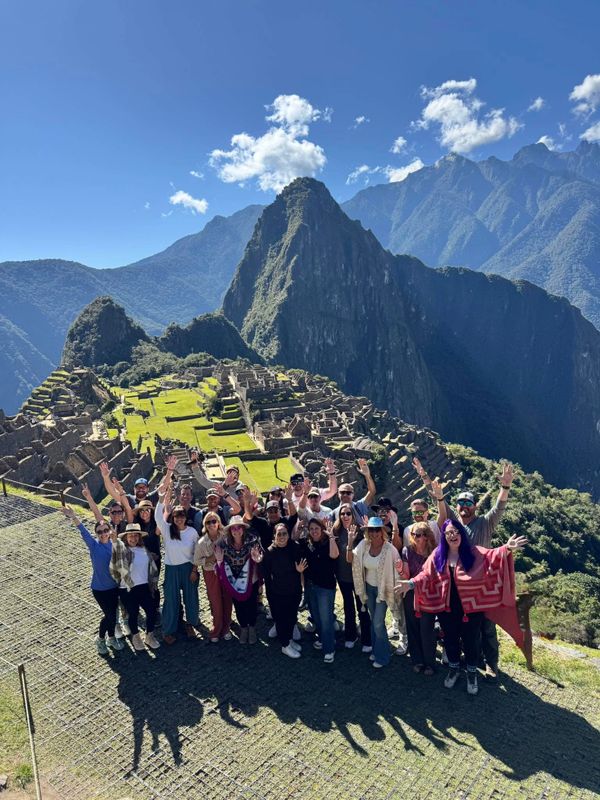 A group of tourists posing happily at Machu Picchu with mountains in the background.