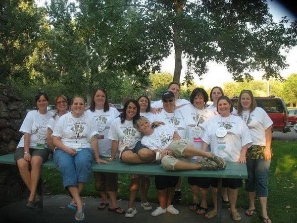 Group of women in matching white shirts posing outdoors on a picnic table.