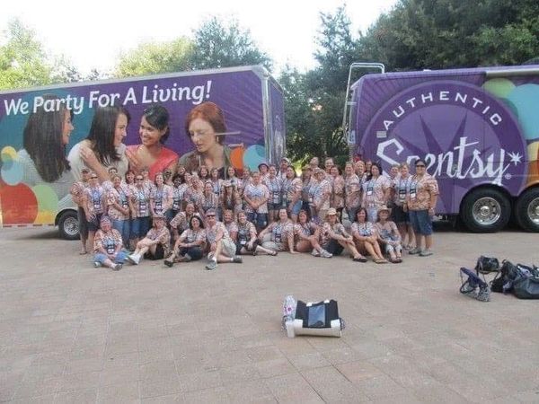 Large group in matching shirts posing in front of colorful Scentsy trucks.