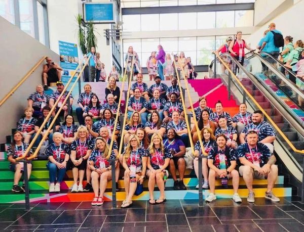 Large group wearing matching shirts sits on colorful stairs inside a building.