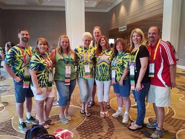 Group of nine people wearing colorful event badges and matching shirts.