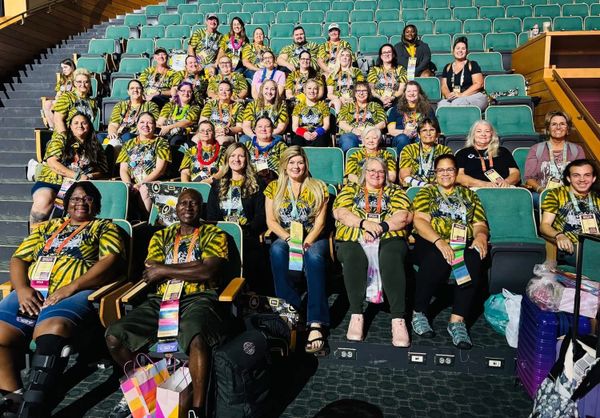 Group photo of people in matching green and yellow tiger-striped shirts seated in an auditorium.