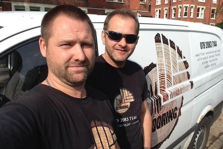 Two men wearing matching black shirts standing by a white van with a logo.