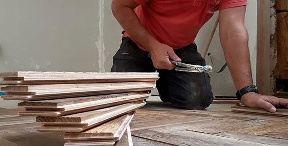 Worker installing wooden flooring inside a room.