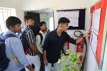 Students closely examining notices pinned on a bulletin board inside a school building.