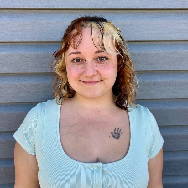 Person with two-toned hair and a handprint tattoo smiles.