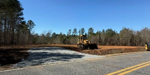 Bulldozer working on clearing land beside a road under clear blue sky.