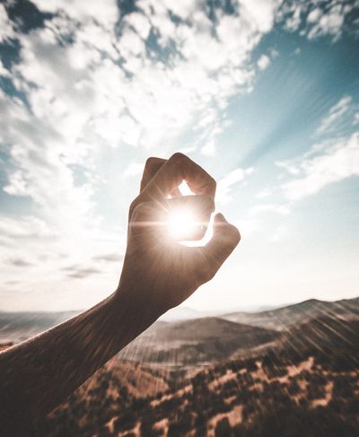 the sun brightly shining through a circle made with someones hand