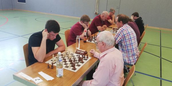 Mehrere Menschen spielen Schach in einer Halle.