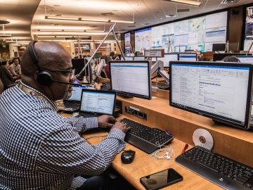 Man working with multiple screens and a headset in a busy office.