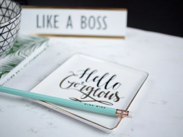 A stylish tray with 'Hello Gorgeous' text and a turquoise pencil on a white marble surface.