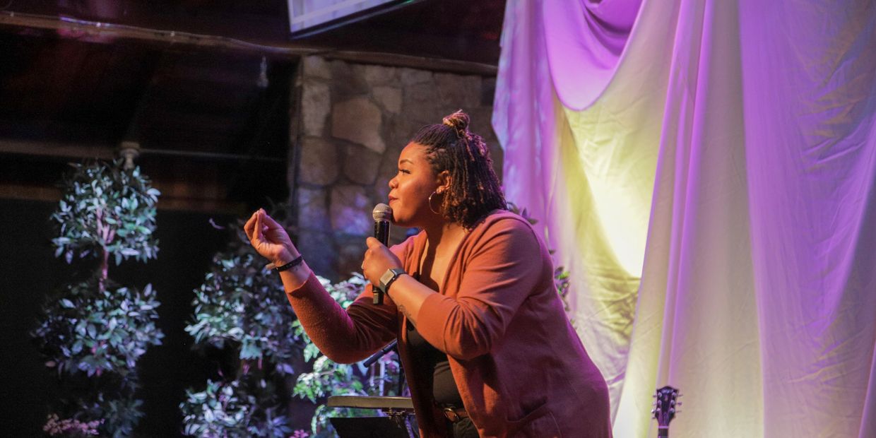 A woman passionately speaks into a microphone on stage with colorful lighting.
