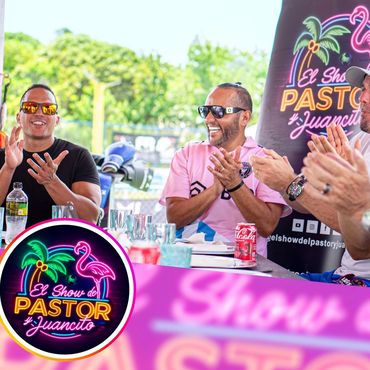 Three men smiling and clapping at an outdoor event with "El Show del Pastor y Juancito" branding.