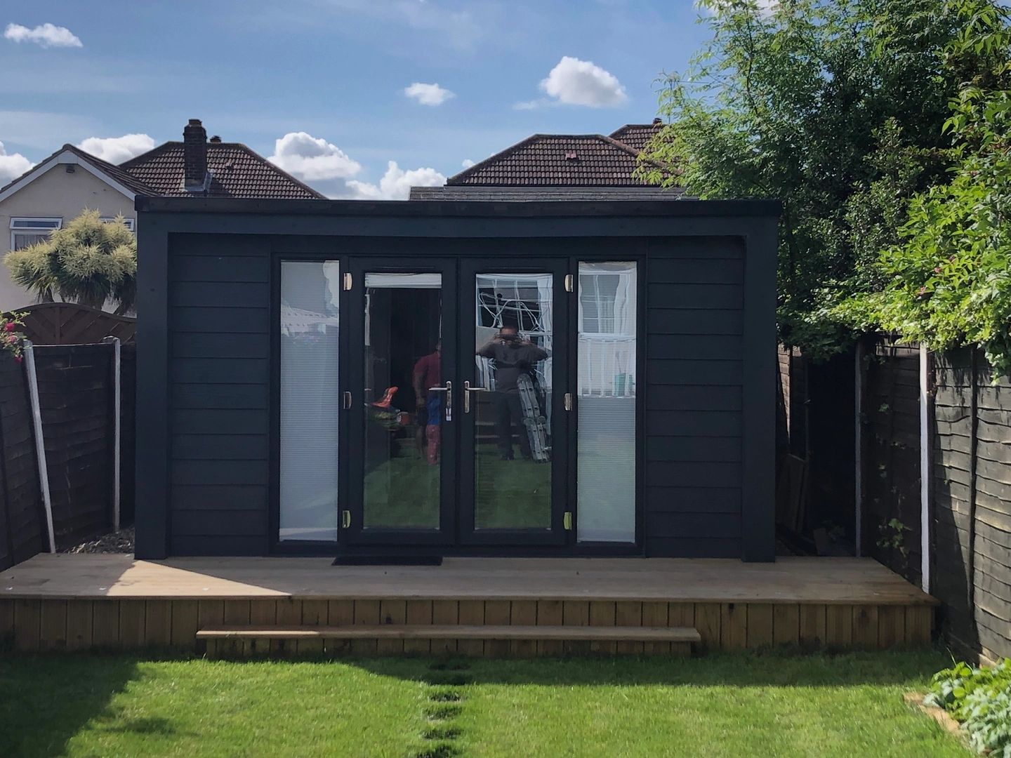 Modern black garden shed with glass doors and wooden deck.
