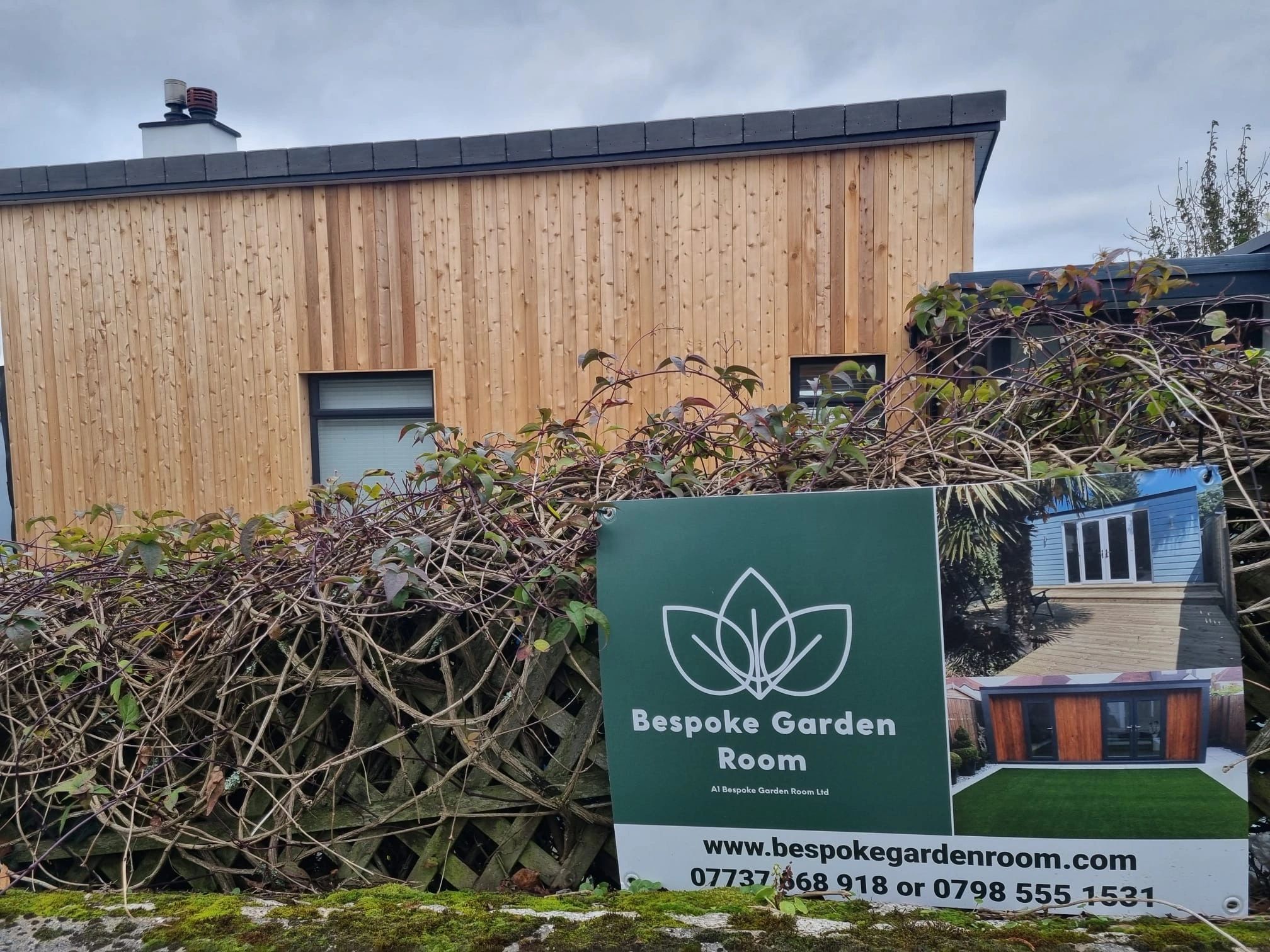 Modern wooden garden room with a promotional sign for Bespoke Garden Room.