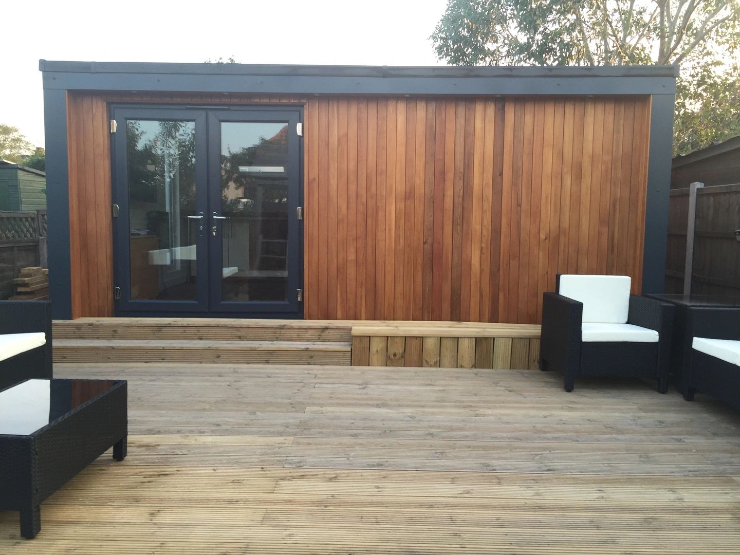 Modern wooden garden room with patio seating and glass doors.